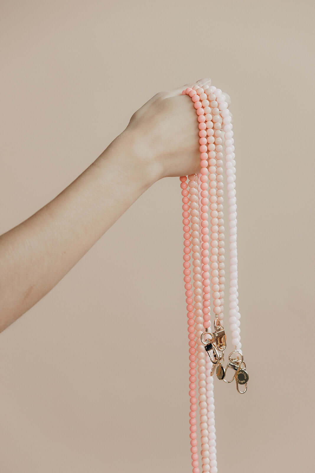 Hand holding several pink and white beaded Aurora PHONE CORD strands with gold-tone clasps.