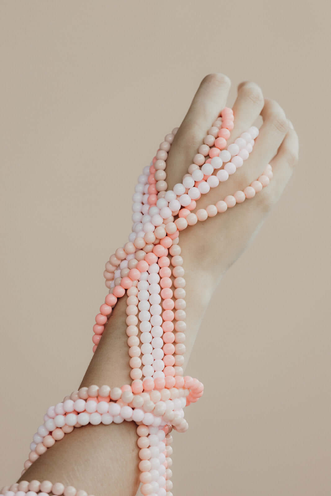 Close-up of pink and white beaded Aurora PHONE CORD strands wound around a wrist and hand.