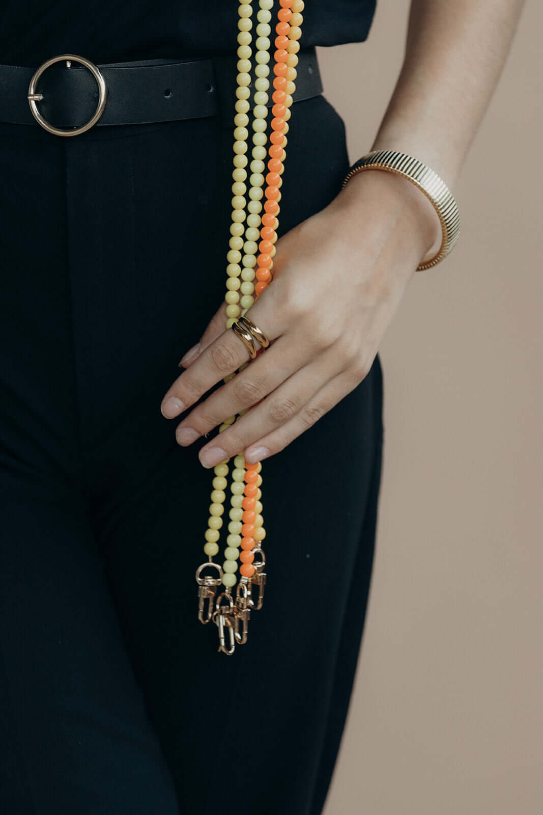 Close-up of a hand with rings beside pale yellow and orange beaded Aurora PHONE CORD strands holding keys.