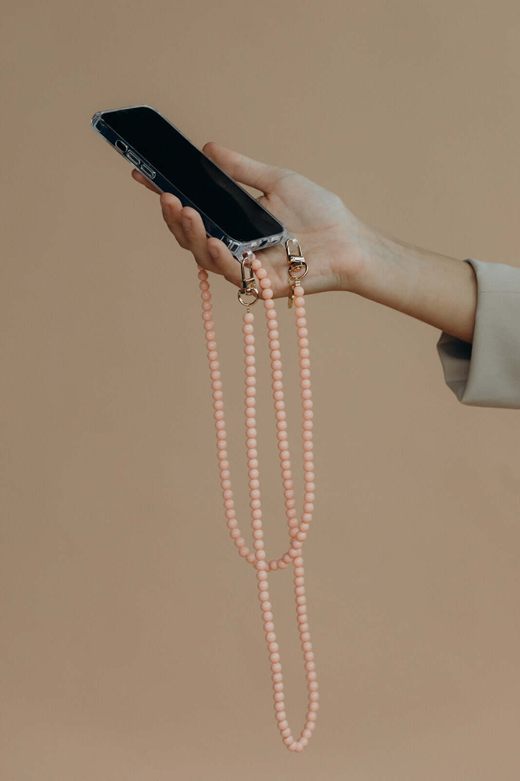 Hand holding a clear phone case attached to a light pink beaded Aurora PHONE CORD.