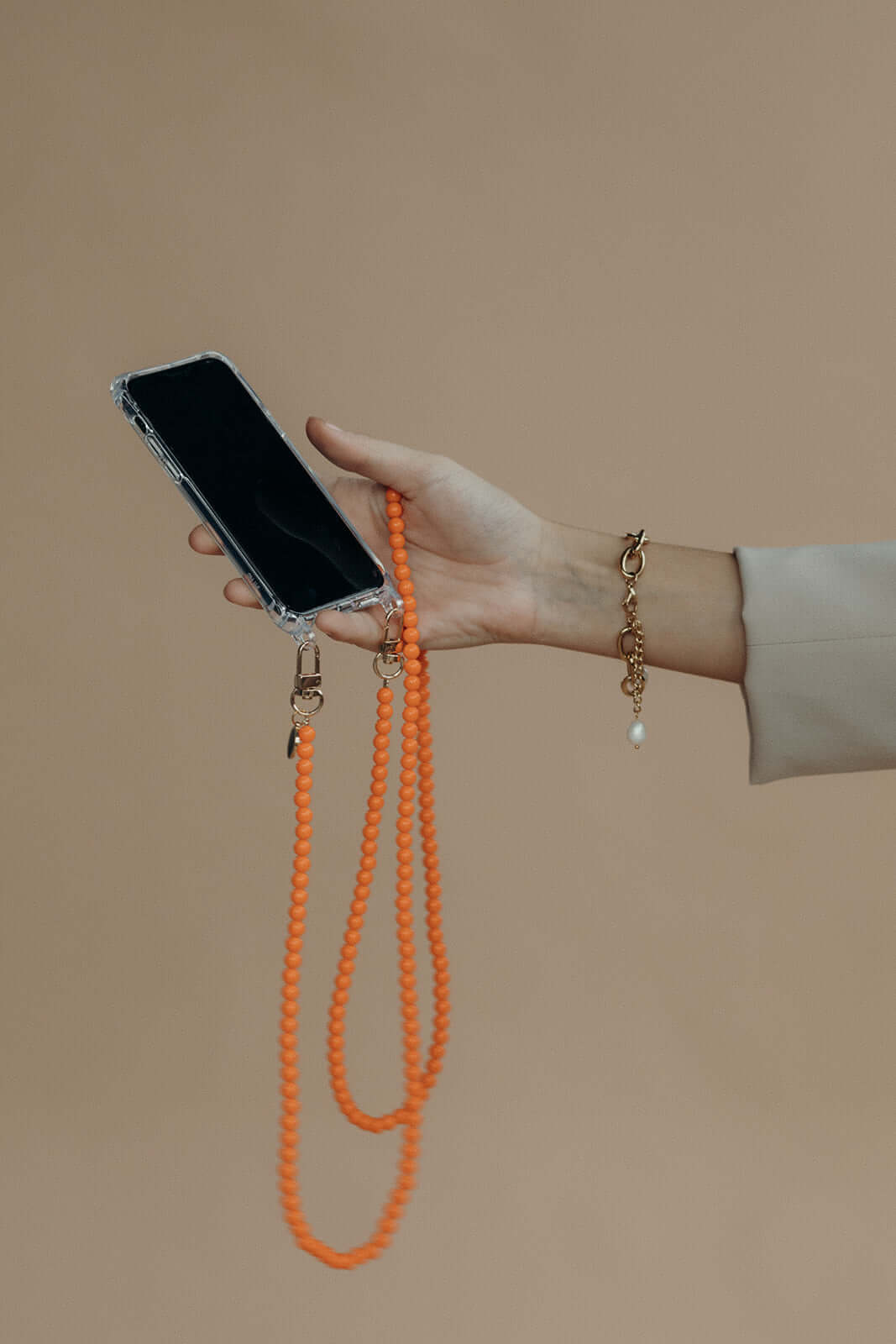 Hand holding a clear phone case attached to an orange beaded Aurora PHONE CORD, gold bracelet on wrist.