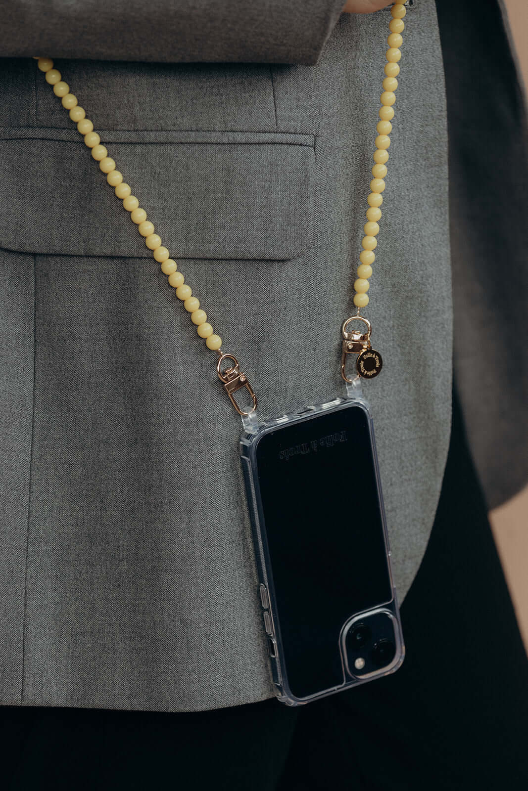 Close-up back view of a pale yellow beaded Aurora PHONE CORD attached to a phone case, model in a gray blazer.