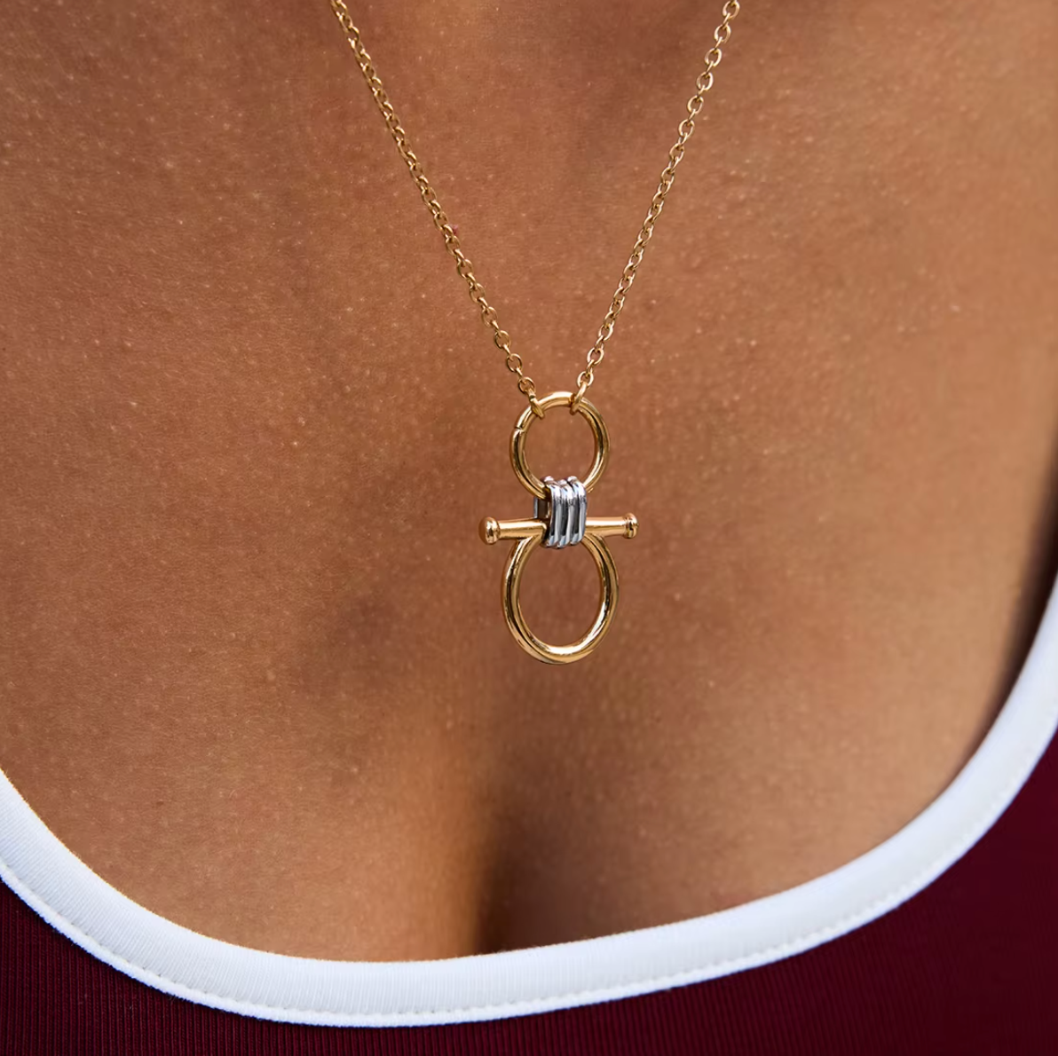 The Averi NECKLACE in close-up at the neckline, showing the gold double-circle pendant and silver ridged bar clasp detail.