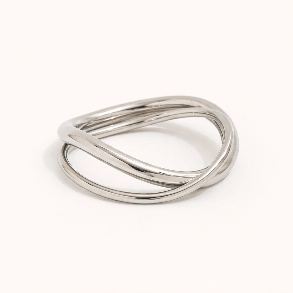 Silver ring made of three interwoven wavy bands, shown at an angle on a cream backdrop — Belance RING.