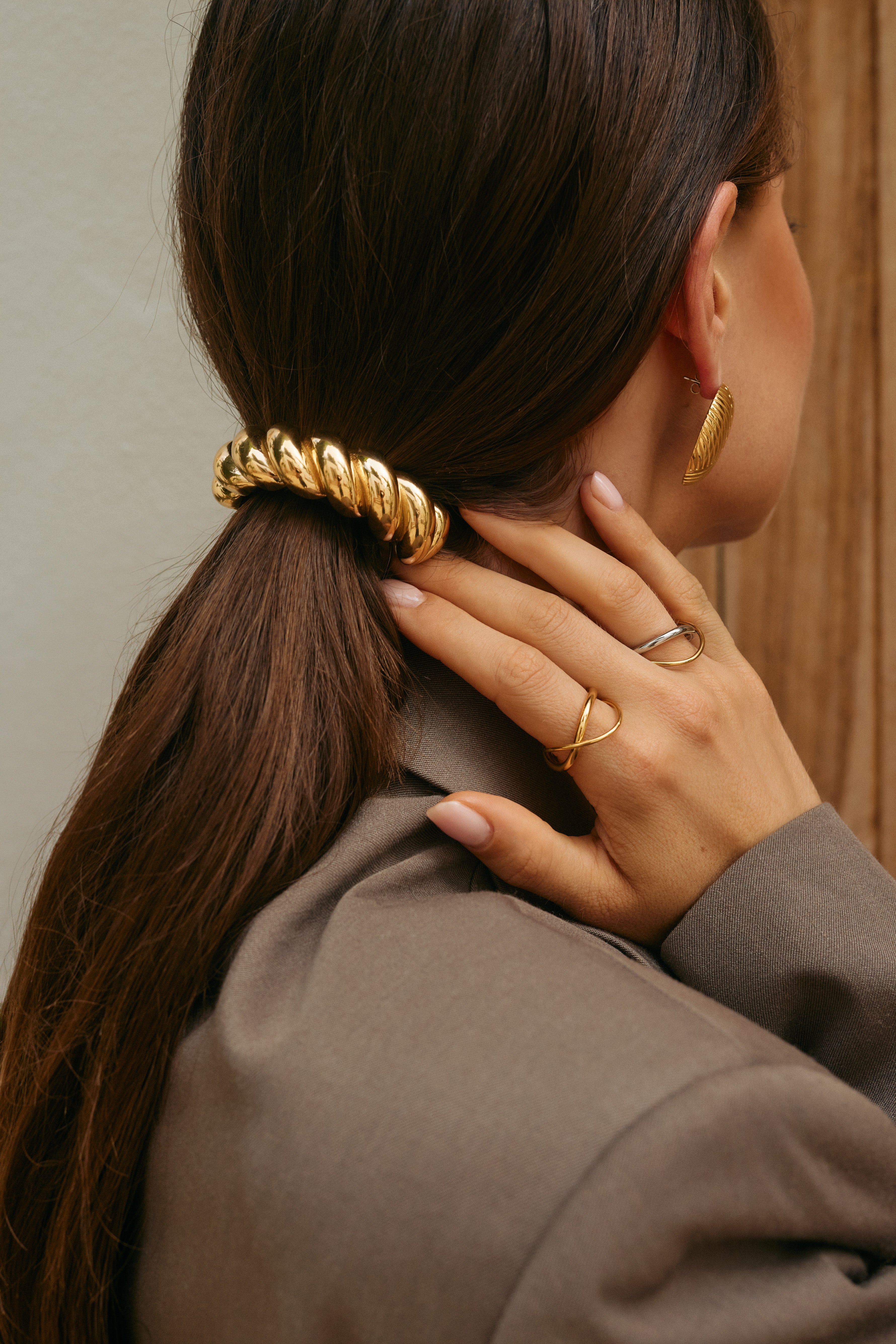Close-up of a hand near the neck wearing the silver interwoven Belance RING stacked with a gold band, near a chunky gold hair clip.