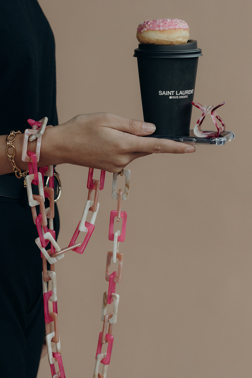 Model holds a coffee cup and donut, wearing the pink and white acrylic Bennie chain on her wrist.