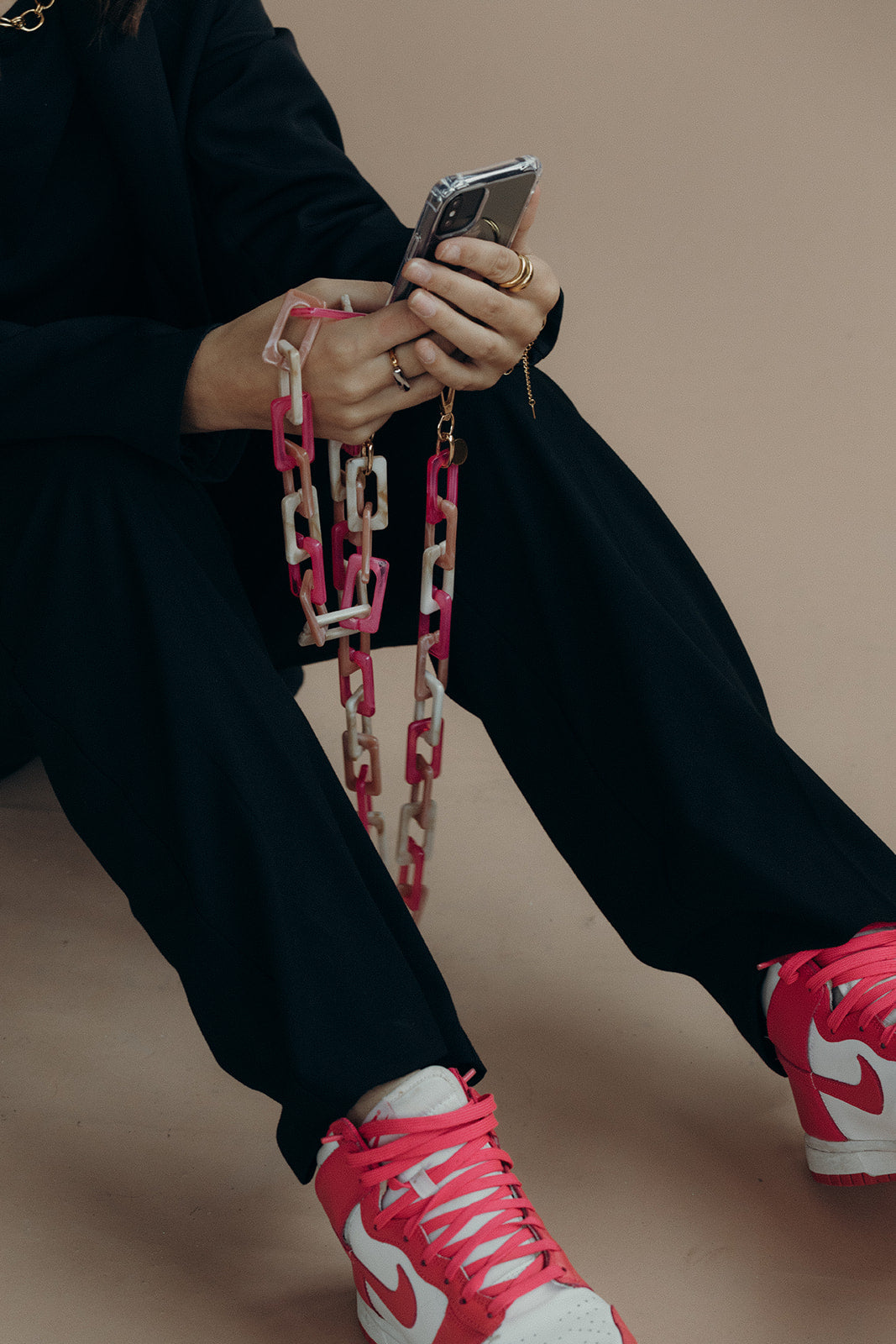 Model holds her phone with the pink and tan acrylic Bennie chain draped over patterned sneakers.