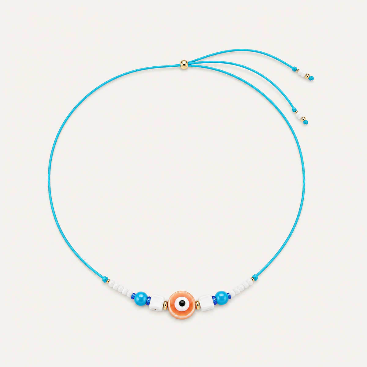 Blue cord Big Eye NECKLACE with beaded glass accents around a peach enamel evil eye charm, laid flat on beige.