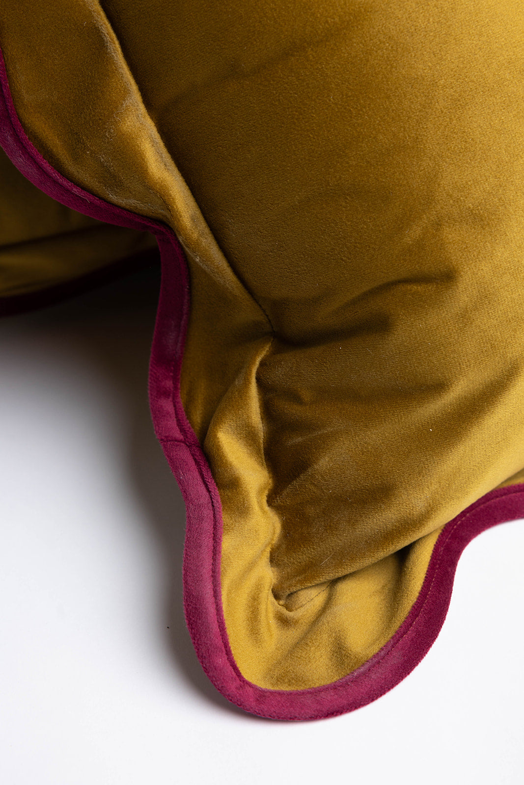 Close-up of the Billie Rectangle Velvet cushion's mustard velvet corner, highlighting its sheen and scalloped burgundy edge.