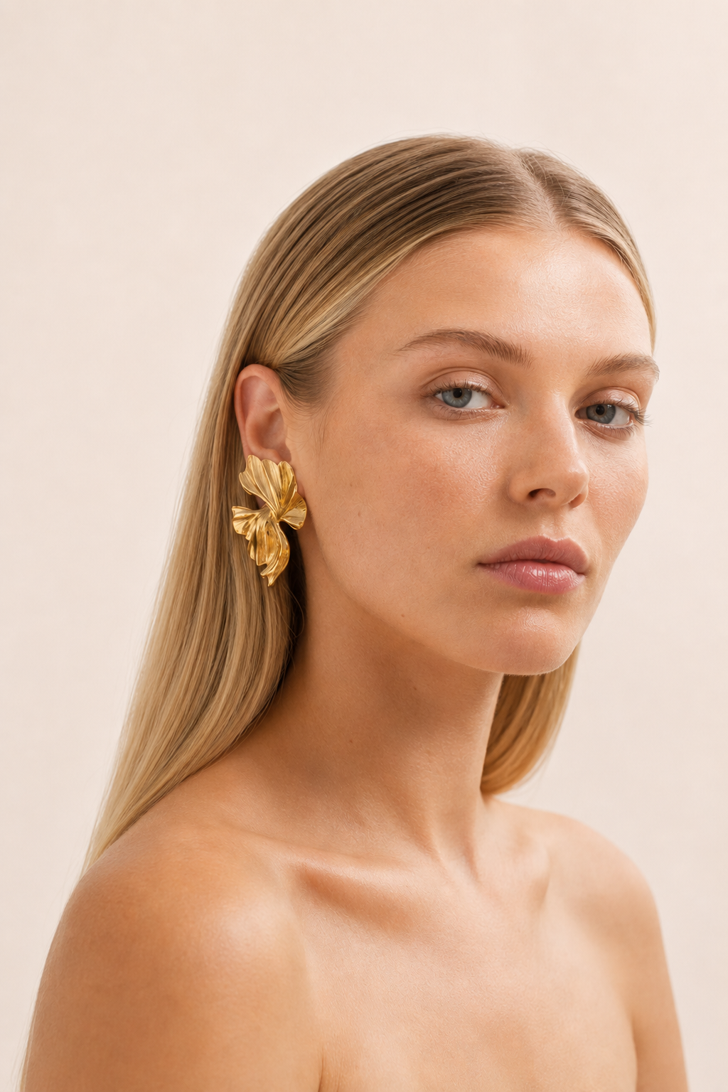 Model with sleek blonde hair wears the gold Botanica EARRINGS, a sculptural textured leaf-petal stud at the ear.