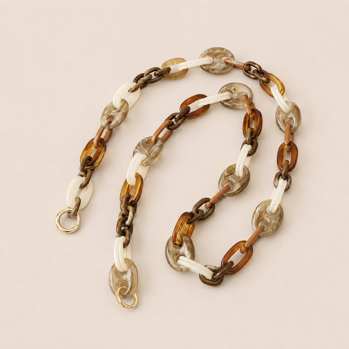 Folie à Trois Bracken long phone chain in brown, tan, white and gray marbled links with gold clasps, coiled on a cream background.
