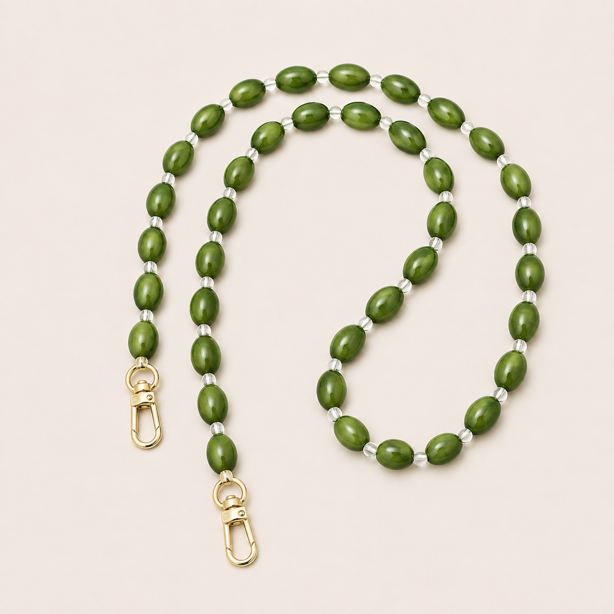 Folie à Trois Bramble long phone chain in olive green oval beads with clear spacers and gold clasps, coiled on a cream background.