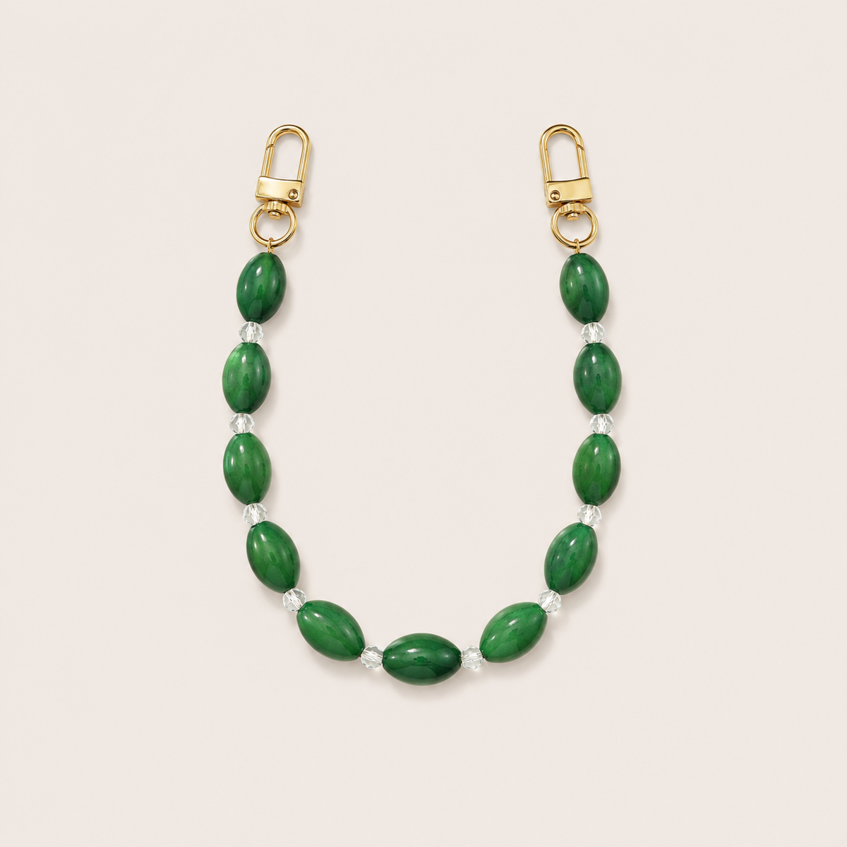 Folie à Trois Bramble short wholesale phone chain in green oval beads with clear glass spacers and gold clasps, laid flat on a cream background.
