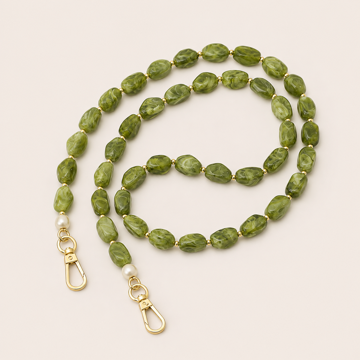 Folie à Trois Briar long phone chain in green marbled nugget beads with gold spacers, pearl accents and gold clasps, coiled on a cream background.