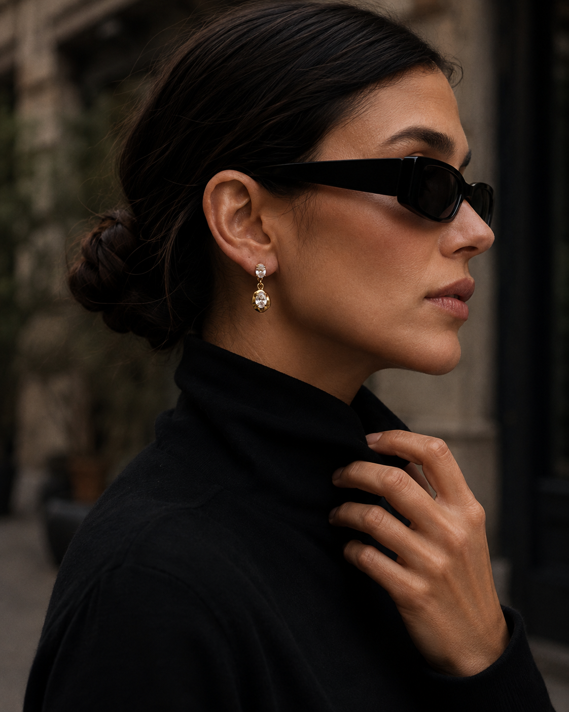 Model in sunglasses and a black turtleneck wears the gold Cameo EARRINGS, a round and oval zirconia sculpted drop.