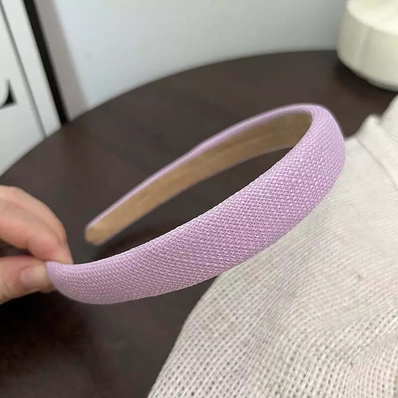 A single solid lilac woven tweed headband held by hand on a dark wood table.