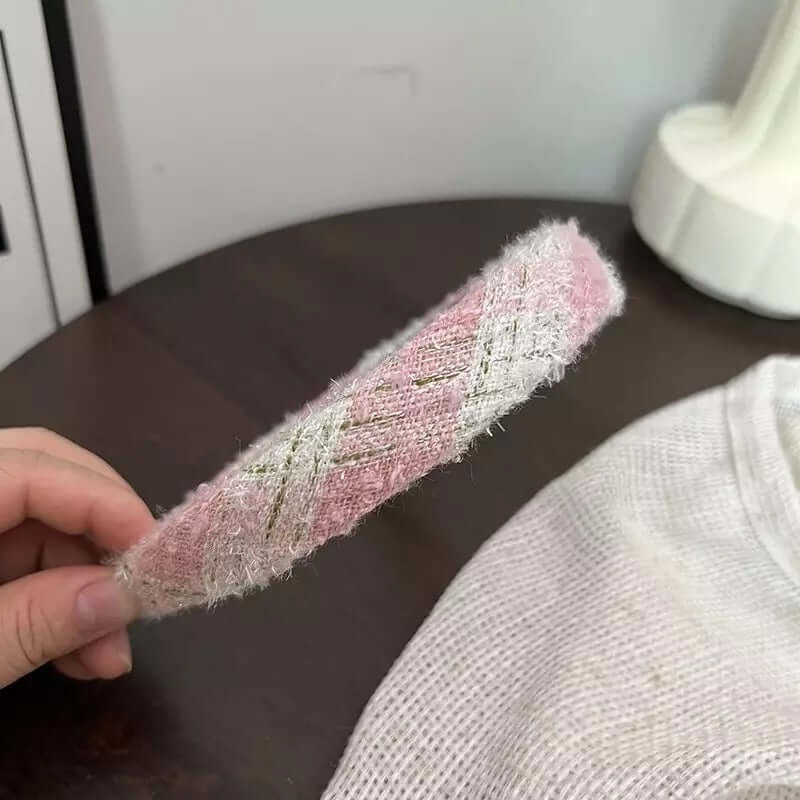 Close-up of a pink and cream diagonal weave tweed headband end, held between fingers.