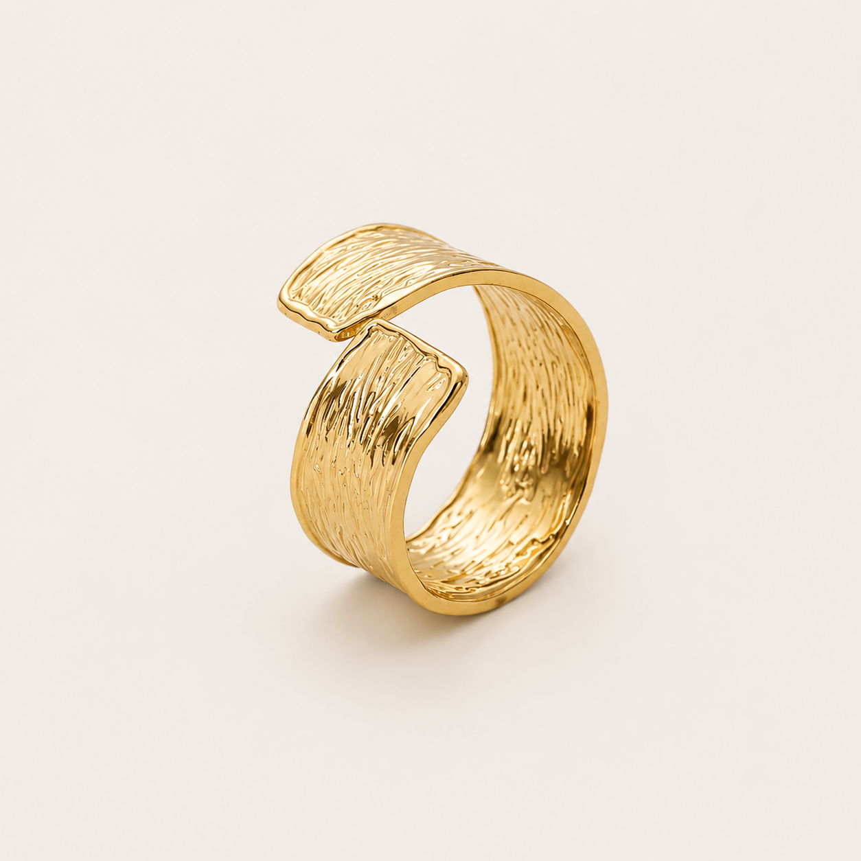 Gold open ring with a wavy, hammered-texture wraparound band, shown in close-up on a cream backdrop — Folie à Trois Cassis RING.