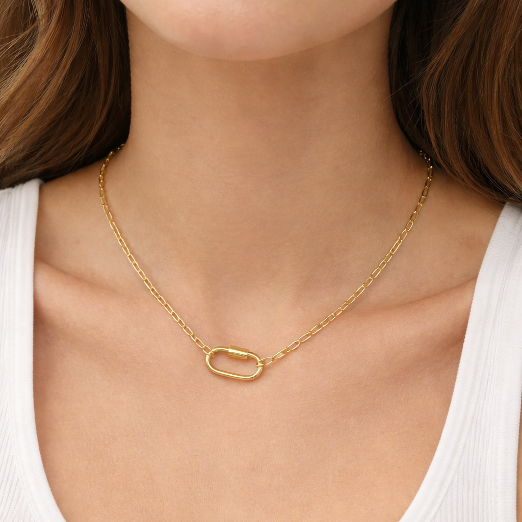 The Chain link Charm NECKLACE worn at the neckline, a gold paperclip chain with an oval carabiner clasp against a white tank top.