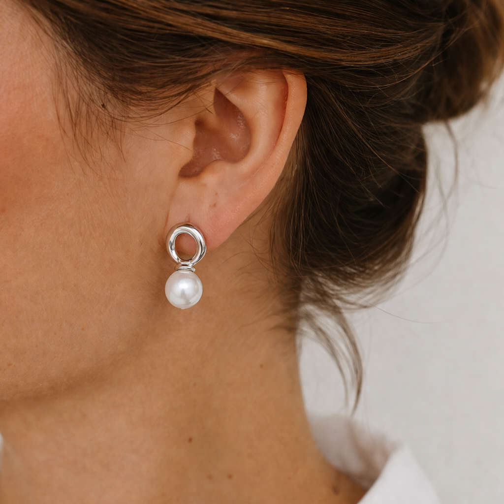 Cher Earrings worn on the ear, the silver open-loop stud with a round pearl resting against the lobe.