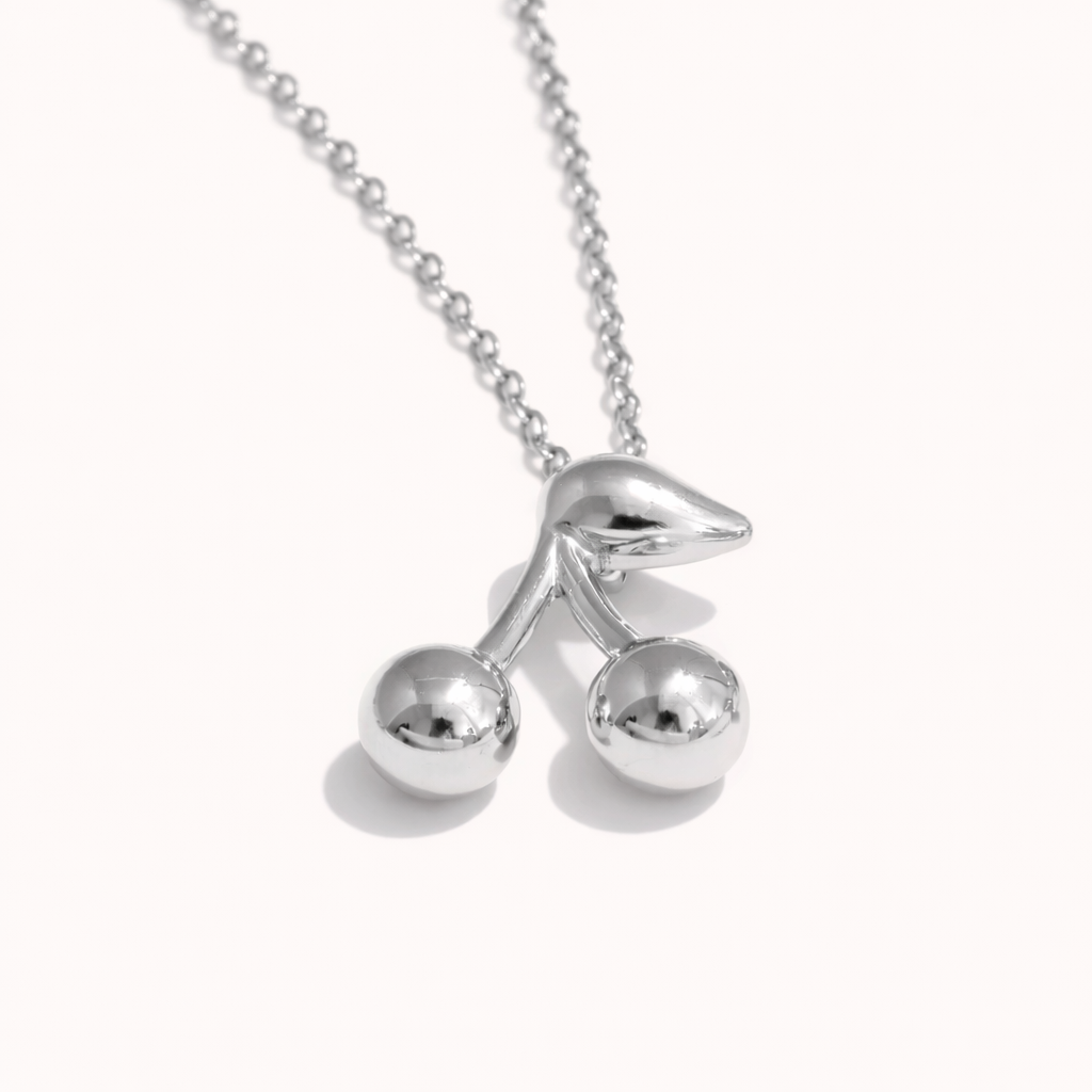 The Cherry On Top NECKLACE in silver, a polished cherry pendant with two round beads and a curved leaf, on a fine chain.