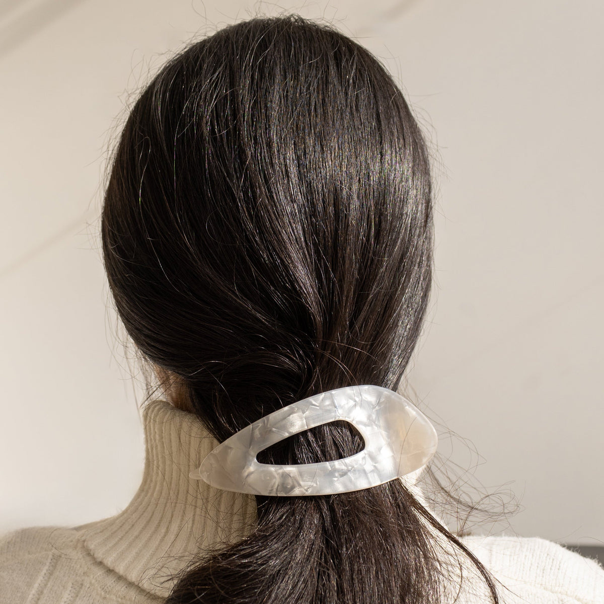 Clara HAIR CLIP in pearly white, worn holding a low ponytail on dark hair, back view.