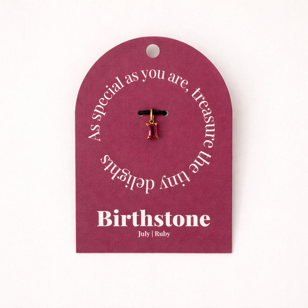 The Classic Drop Birthstone Charm in red ruby hangs from a black cord on a maroon gift card reading Birthstone, July, Ruby.