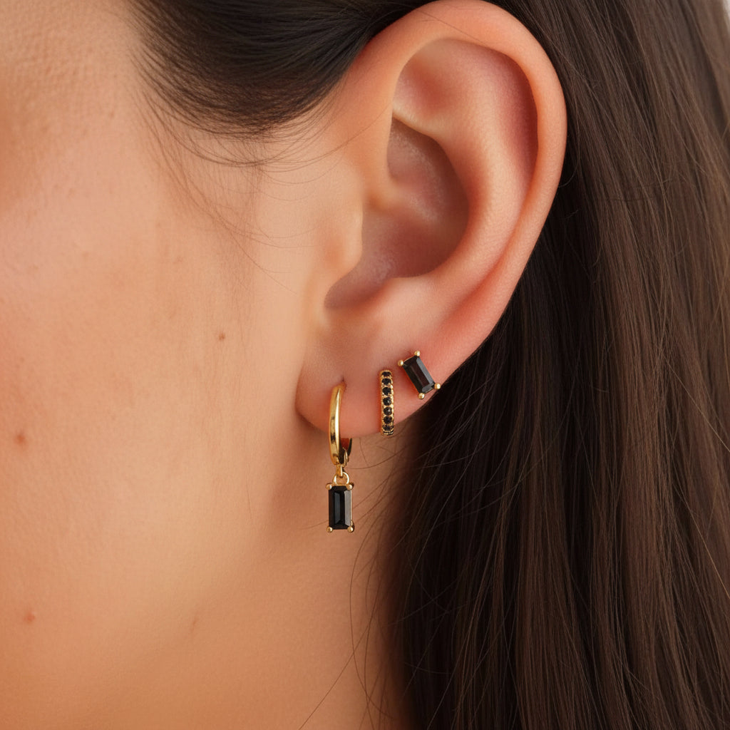 A model wears the Classic Drop SET in black onyx, layering a baguette stud, dangle hoop, and pavé hoop along the ear.
