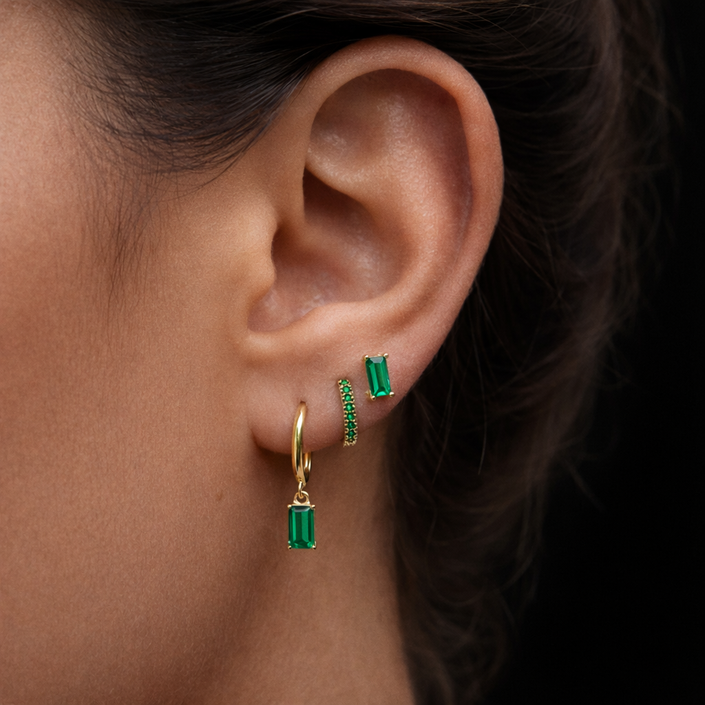 A model wears the Classic Drop SET in emerald green, combining a baguette stud, dangle hoop, and pavé hoop along the ear.