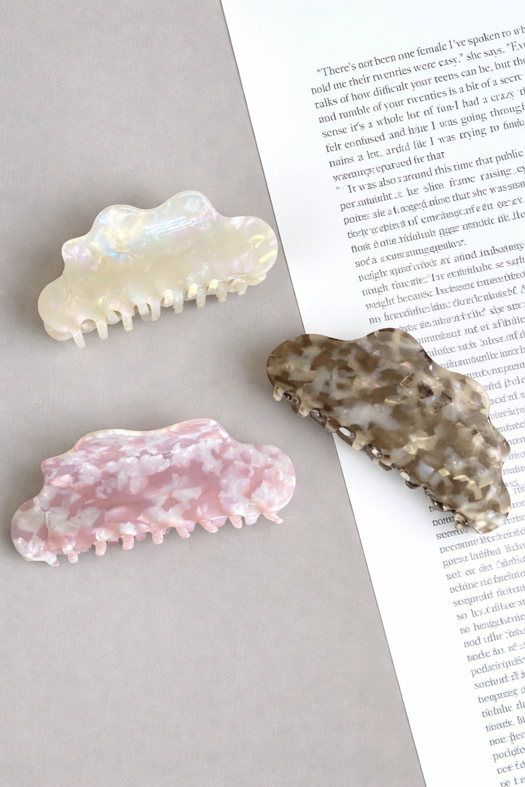 Cloudy Day HAIR CLIP's cream, pink and grey cloud clips styled on an open book with a taupe background.