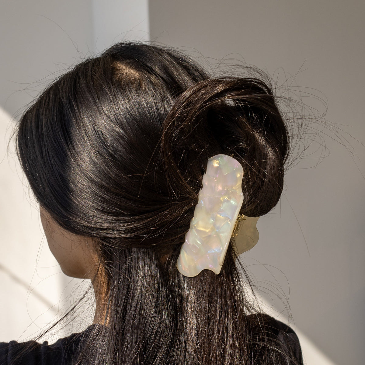 Cloudy Day HAIR CLIP's cream iridescent cloud clip worn upright in a dark hair bun, in sunlight.