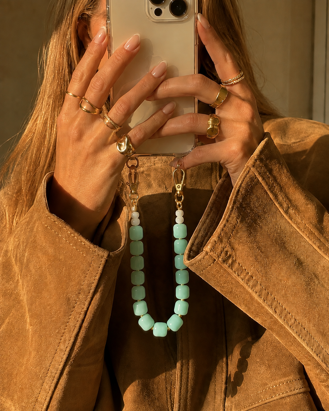 Woman in a suede jacket holds her phone by a mint green beaded chain, gold rings on her fingers — Folie à Trois Cora phone chain