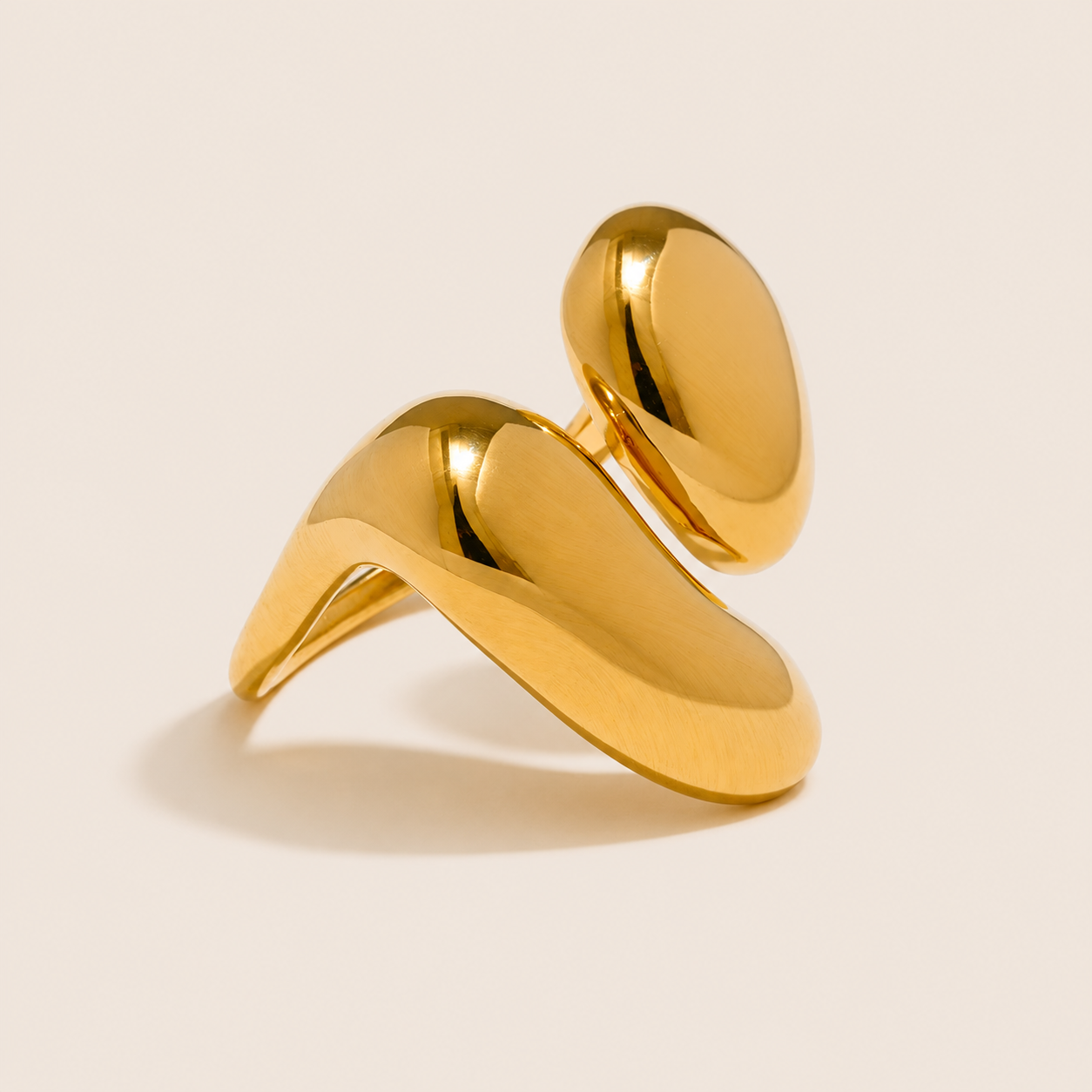 Gold bypass ring with two glossy teardrop-shaped domes wrapping around each other, on a cream backdrop — Folie à Trois Côte d'Été RING.