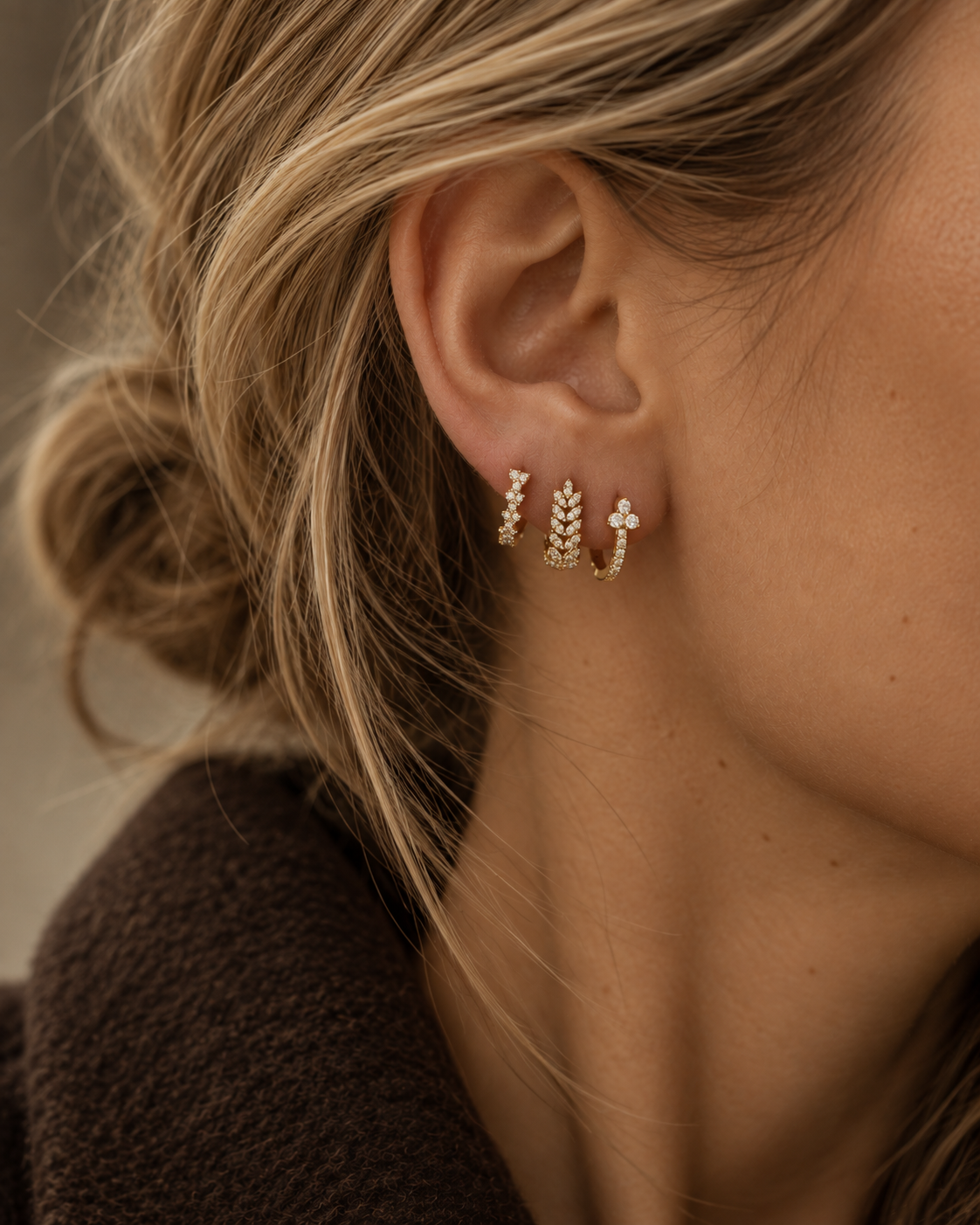 Model with a low bun wearing the gold Daisy SET on one ear: a pavé hoop, a leaf-shaped pavé hoop and a flower-top hoop.