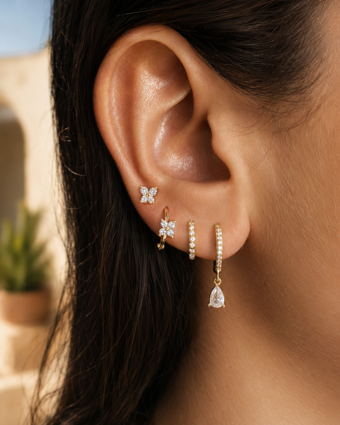 A model wears the four-piece Deanna SET gold earrings in clear stones stacked along her ear, including a hoop with a pear-cut drop charm.