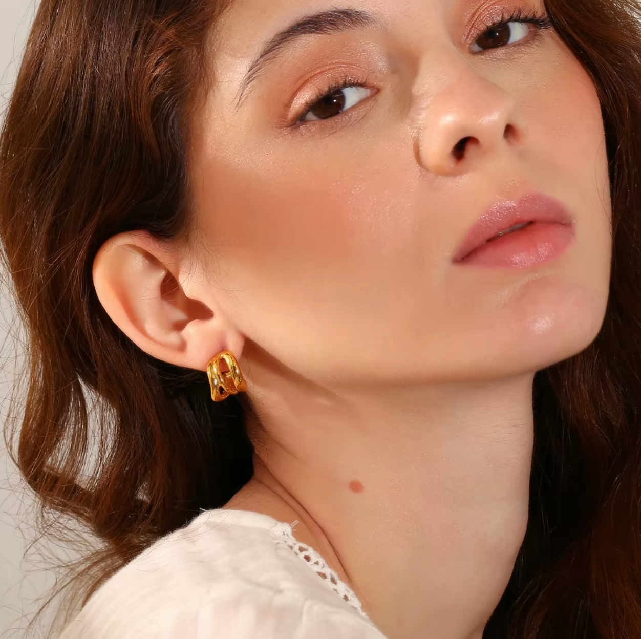 Delphi Earrings worn in gold on the ear, the twisted chunky hoop catching light against loose waves.