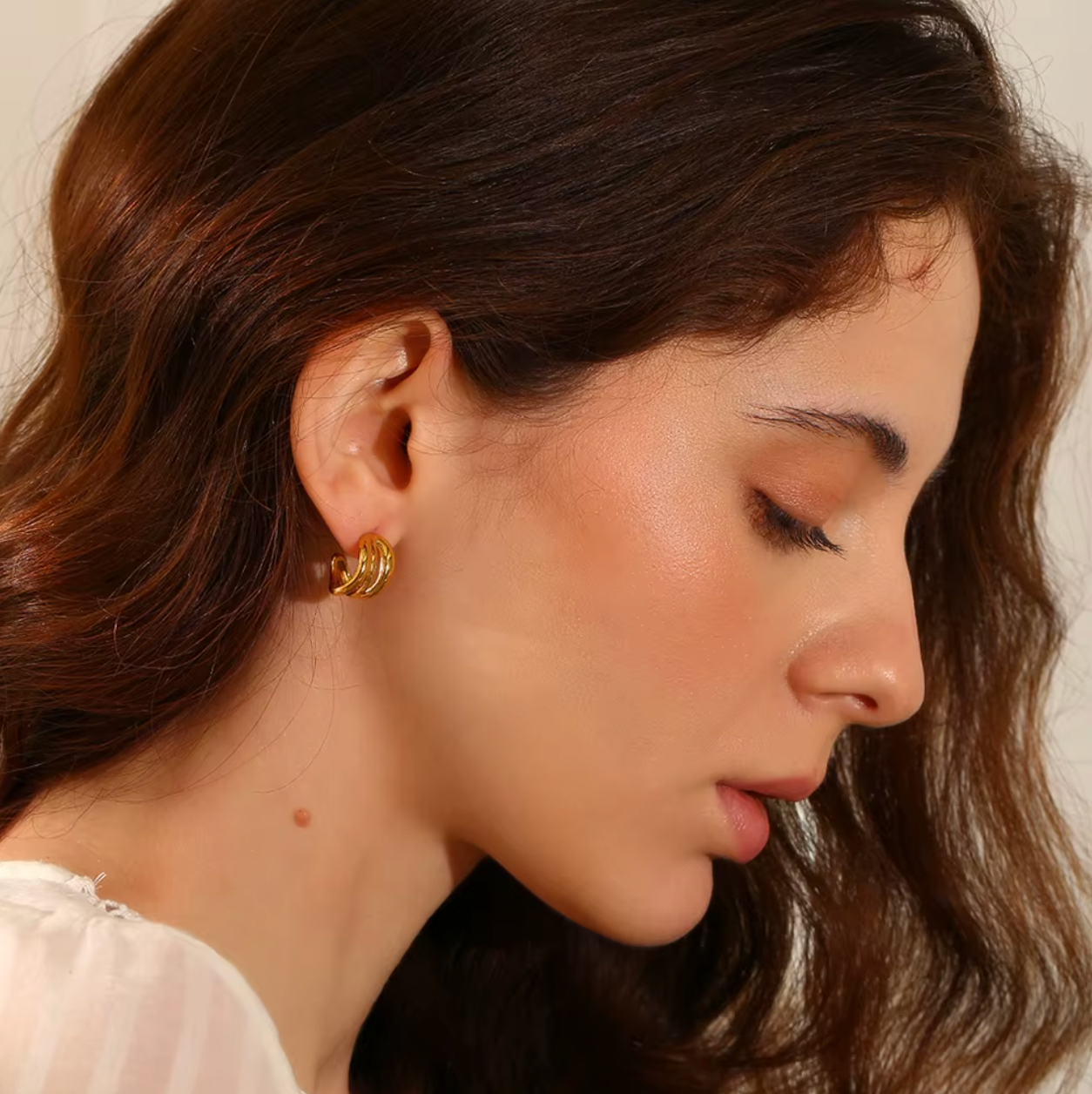 Delphi Earrings worn in profile, the gold interlaced hoop shown close on the ear with soft waves framing the face.