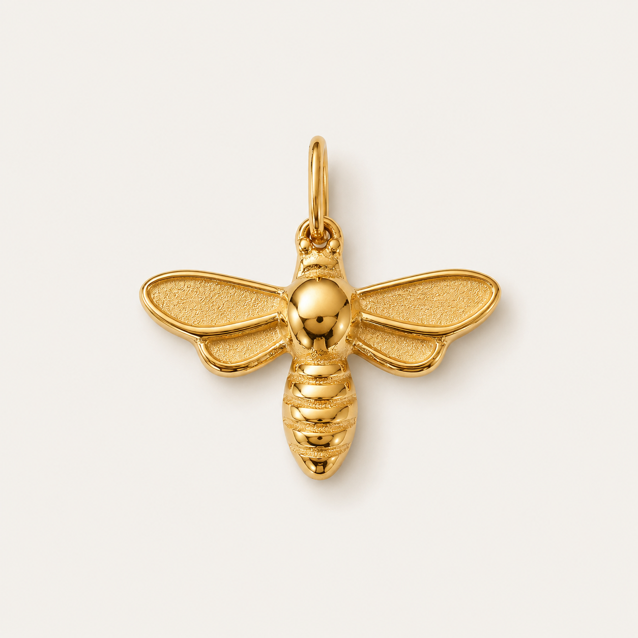 The Dragonfly CHARM in gold, a bee-shaped pendant with textured wings and a ribbed body, shown in close-up studio photography.
