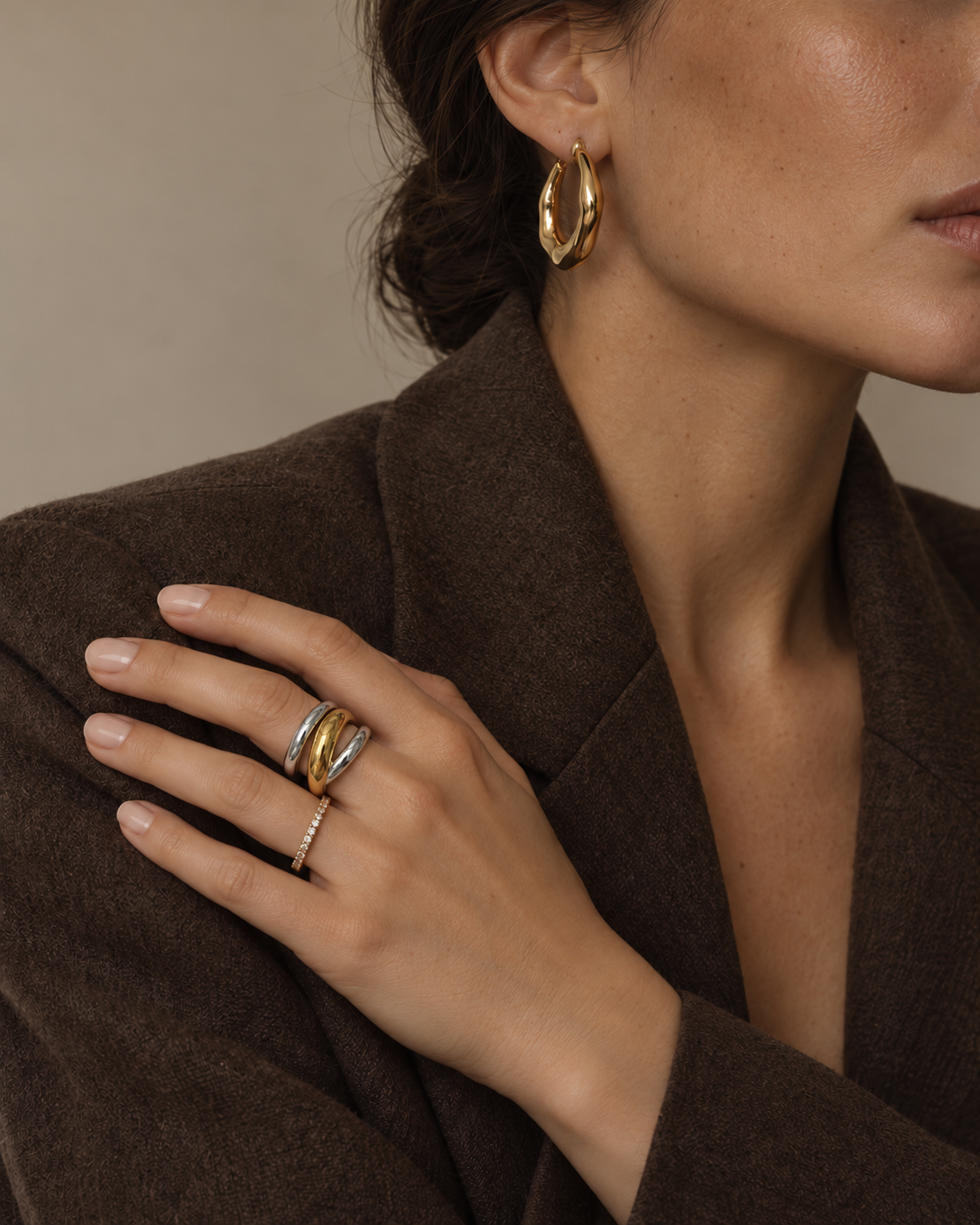 Model in a brown blazer and gold hoops rests her hand on her shoulder, wearing the two-tone Duetto RING — Folie à Trois