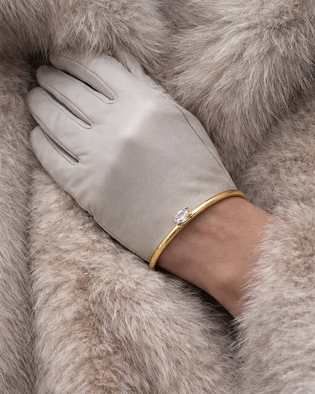 Electric Frost BRACELET in gold worn over a grey leather glove, model wrapped in a soft faux fur coat.
