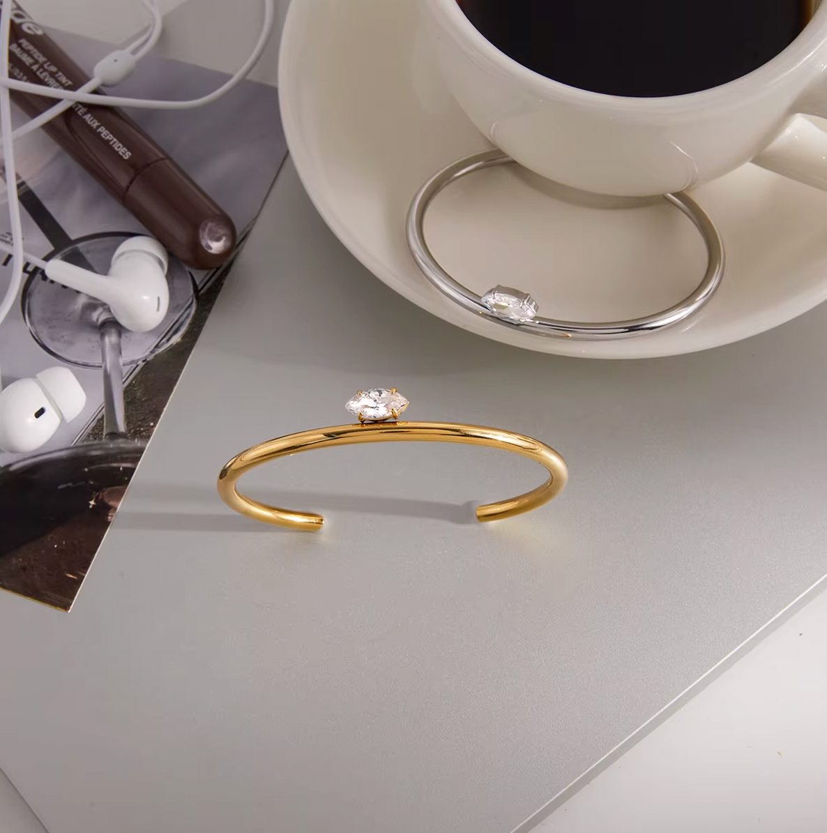 Electric Frost BRACELET in gold styled on a desk beside a coffee cup, earbuds, and an open magazine.