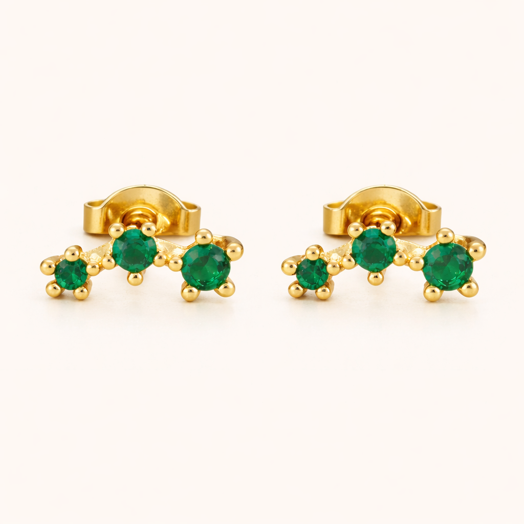 Emerald-green climber earrings featuring three round emerald stones set in a curved gold row, shown as a matching pair.