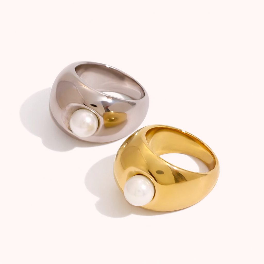 Gold and silver Elka RING styles, each a chunky dome band set with a single pearl, shown together on a cream backdrop.
