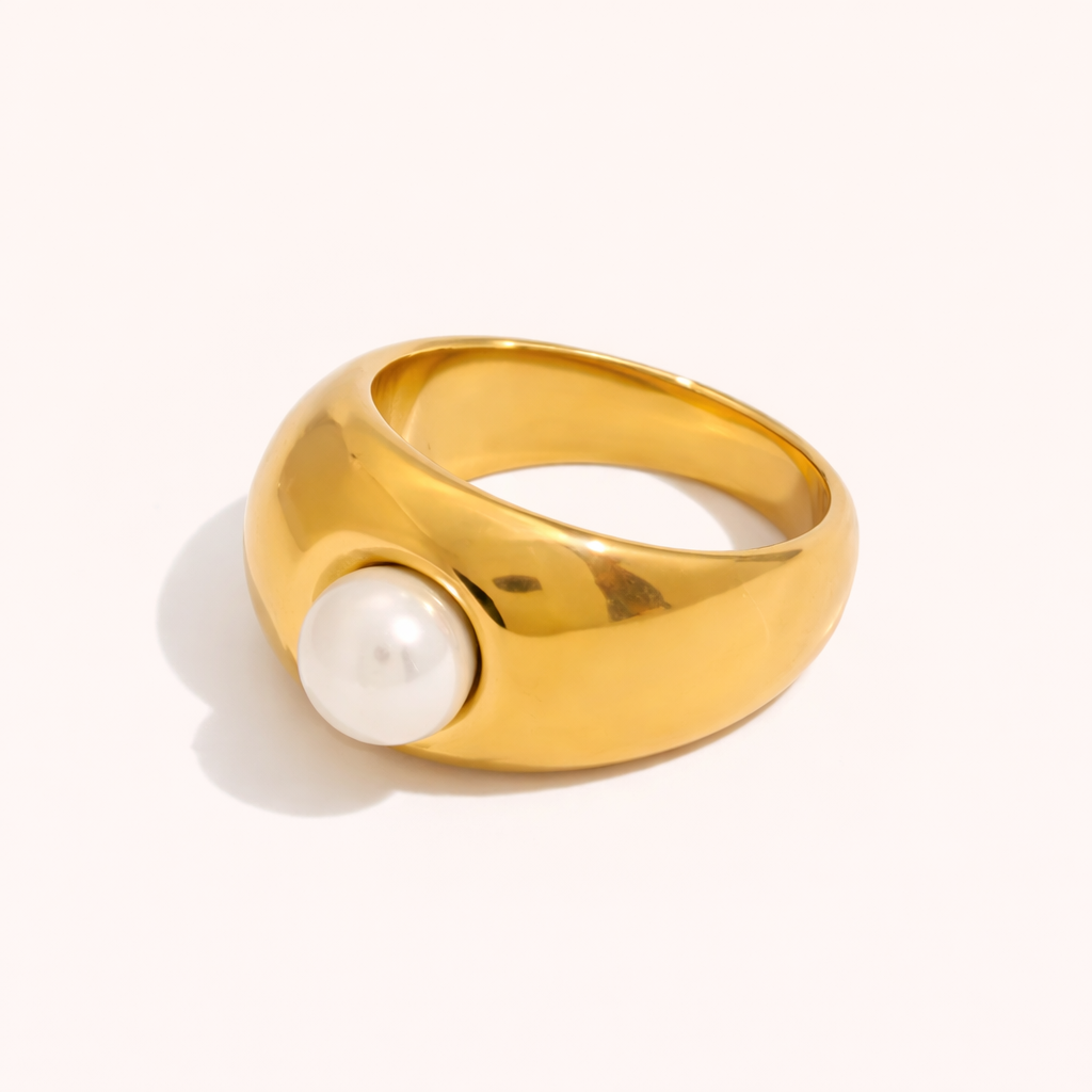 Chunky gold dome ring set with a single pearl, shown at an angle on a cream backdrop — Elka RING.