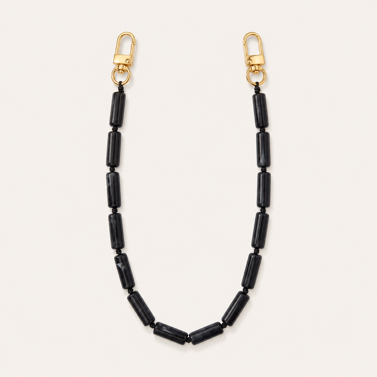 Black tube-bead phone chain with gold lobster clasps laid flat on cream — Folie à Trois Elowen wholesale phone chain
