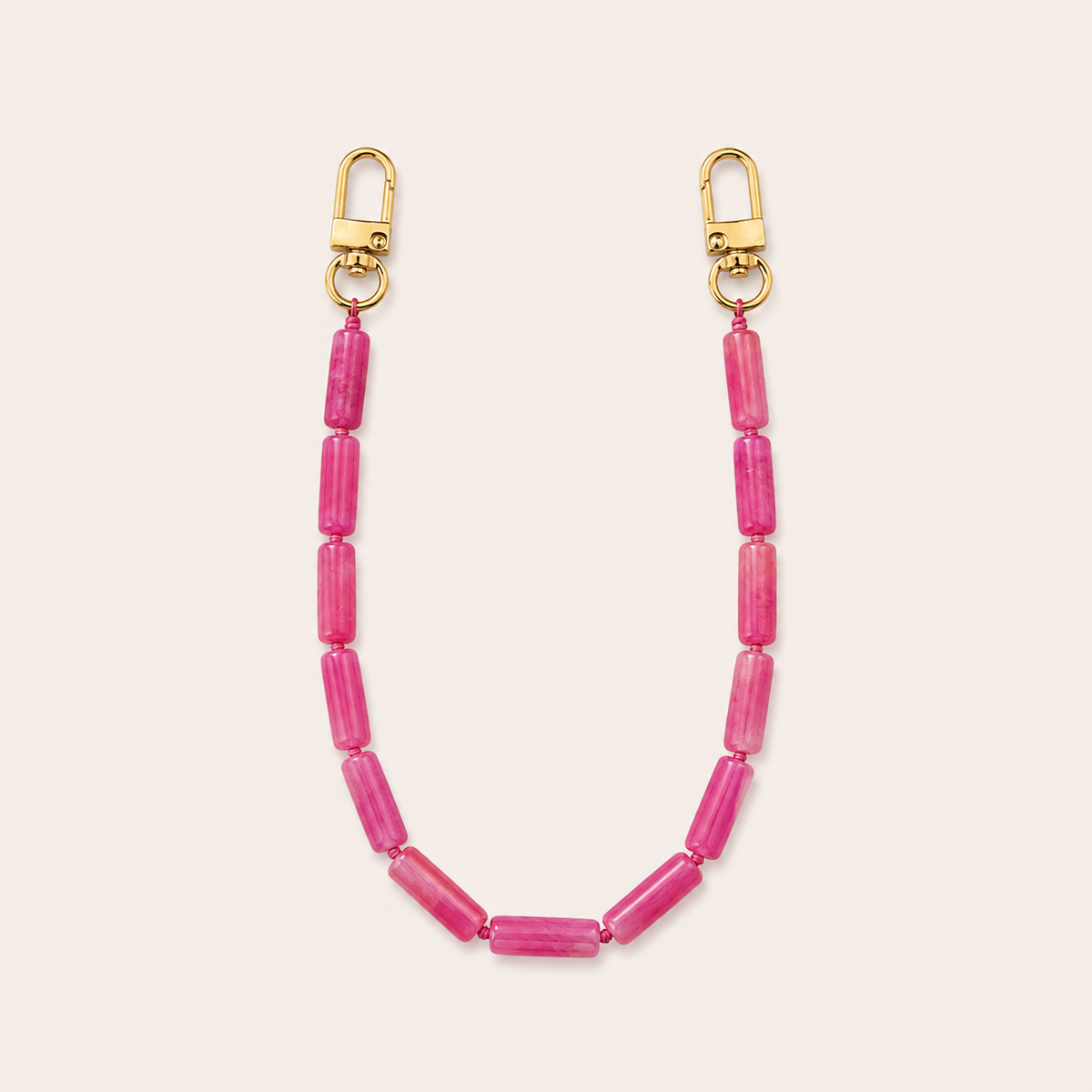 Magenta pink tube-bead phone chain with gold lobster clasps laid flat on cream — Folie à Trois Elowen wholesale phone chain