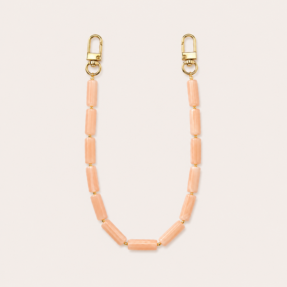 Peach tube-bead phone chain with gold lobster clasps laid flat on cream — Folie à Trois Elowen wholesale phone chain