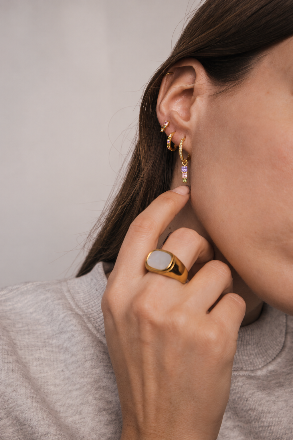 Model wears the Folie à Trois Fashion House SET stacked along the ear in a lilac colorway, her hand with an opal signet ring raised to her neck.