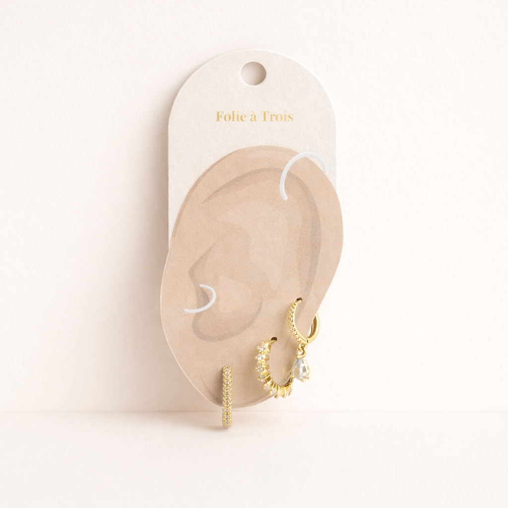 The Fia SET is displayed on a branded card shaped like an ear, showing the gold pieces and teardrop charm.
