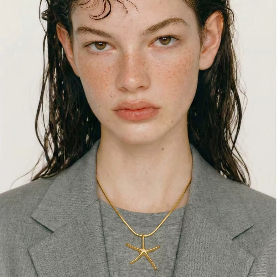 The Fiji NECKLACE worn close-up on a gray tee, the model's wet hair framing her face in a straight-on portrait.